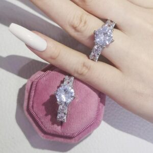 Bagues Big Diamond Ring argentées à grande pierre ronde, l’une portée sur un doigt et l’autre sur un support rose